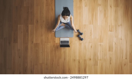 High angle view of young Asian woman practicing yoga and meditation at home sitting on floor in living room in lotus position with laptop and dumbbell. Mindful meditation and wellbeing concept - Powered by Shutterstock