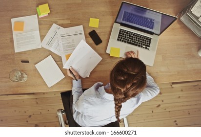 High Angle View Of An Young Brunette Working At Her Office Desk With Documents And Laptop. Businesswoman Working On Paperwork.