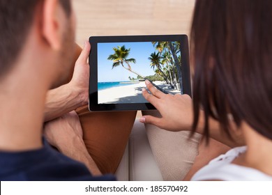 High Angle View Of Young Couple Looking At Photos On Digital Tablet Together At Home
