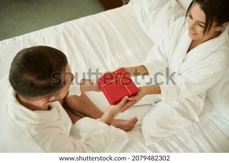High angle view of a young couple in love holding a red gift box for a special occasion. Birthday, marriage anniversary concept. Loving married couple giving each other gifts for Valentine's Day