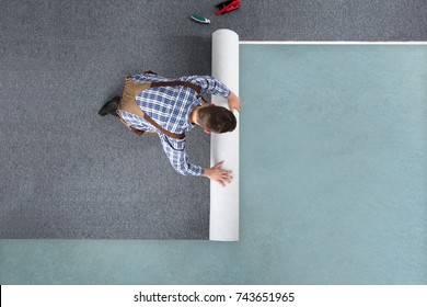 High Angle View Of Young Male Worker In Overalls Rolling Carpet On Floor At Home