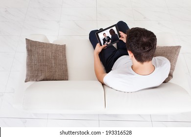 High Angle View Of Young Man Watching Movie On Digital Tablet In Living Room