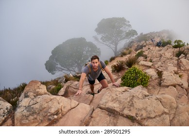 High angle view of a young man carefully climbing up rocks on a mountain nature trail