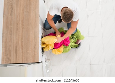 High Angle View Of Young Man Putting Clothes In Washing Machine