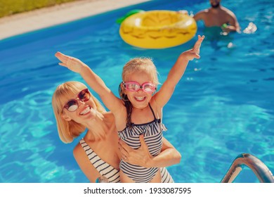 High angle view of young mother having fun playing with her daughter in the swimming pool, enjoying hot sunny summer day outdoors and relaxing while on a vacation - Powered by Shutterstock