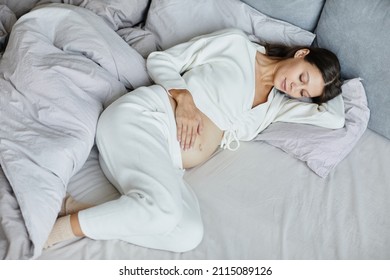 High angle view of young pregnant woman in pyjamas lying in her bed during her leisure time - Powered by Shutterstock