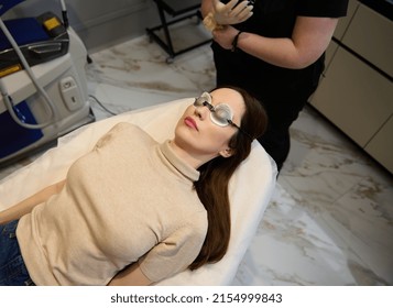 High angle view of a young pretty European woman wearing UV protective goggles and lying down on the daybed in a wellness spa clinic