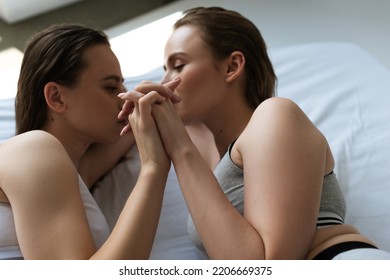 High Angle View Of Young Same Sex Couple Holding Hands While Lying On White Bedding