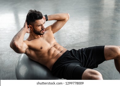 high angle view of young sportsman with bare chest doing abs exercise on fitness ball at gym 