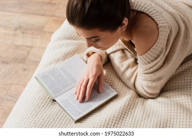 High Angle View Of Young Woman Reading Book While Resting On Bed At Home