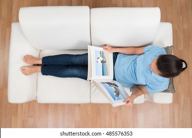 High Angle View Of Young Woman Looking At Photo Album On Sofa