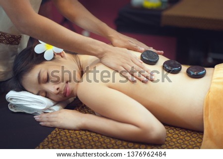 High angle view of young woman lying down on massage bed with traditional hot stones along the spine at spa and wellness center