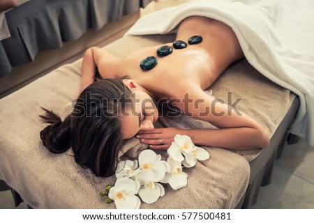High angle view of young woman lying down on massage bed with traditional hot stones along the spine at spa and wellness center 