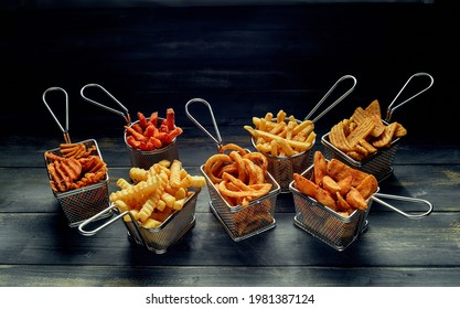 High angle of wedge and sweet potatoes with waffle and crinkle fries in stainless baskets on wooden table