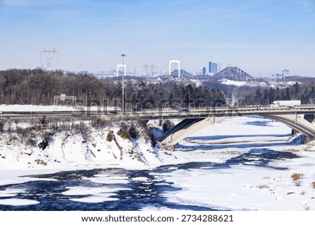 High angle winter view of bridge over the partly frozen Chaudière river, with the Pierre-Laporte and Quebec bridges in the background, Lévis, Québec, Canada