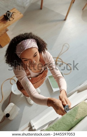 High angle of young African American businesswoman using paintroller while coloring wall of cafe in green during renovation works