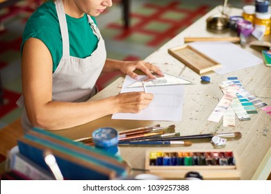 High Angle Of Young Woman Drafting Sketch With Pencil For Art And Craft Project Sitting At Wooden Table In Workshop