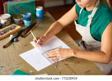 High Angle Of  Young Woman Drafting Sketch With Pencil For Art And Craft Project Sitting At Wooden Table In Workshop