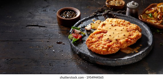 High angle of yummy fried breaded veal escalope with golden crust garnished with creamy spicy yellow sauce and fresh vegetables on wooden table