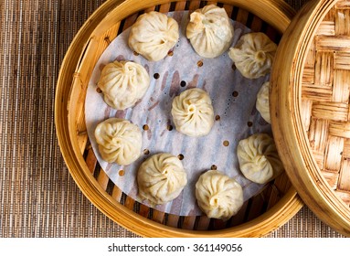 High angled view of cooked dumplings inside of bamboo steamer with lip partially off. 