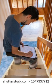 A High Angled View Of A Home Inspector Standing On Stairs Inside A Family Home, Taking Notes During An Indoor Environmental Quality IEQ Assessment.