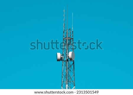 High antenna tower used for various signals. Telecommunication tower with antennas and satellite dishes on the clear blue sky.