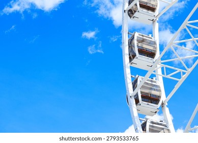 high cabin frame work large Ferris wheel structure amusement carousel set against a clear blue sky with scattered white clouds