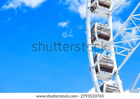 high cabin frame work large Ferris wheel structure amusement carousel set against a clear blue sky with scattered white clouds