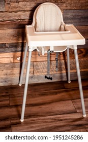 High Chair For Children In The Restaurant. An Empty White Plastic Baby Chair On A Brown Insulated Background In A Cafe.