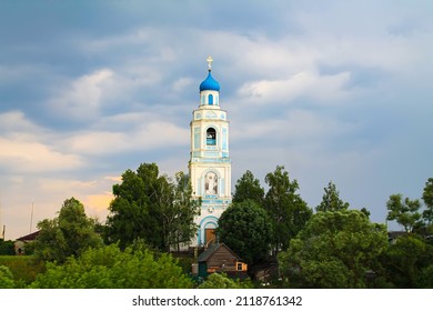 High Church Bell Tower Among Trees Against Blue Sky