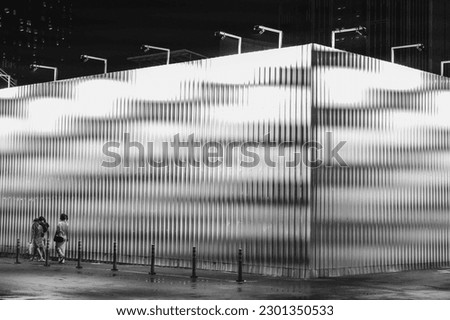 High contrast of black and white metal sheet wall and walking people  at night.