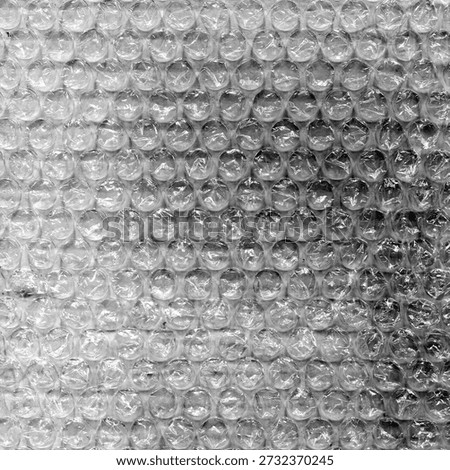 High contrast bubble wrap texture on black background with glowing light reflections. Abstract plastic pattern, futuristic industrial surface, dramatic lighting, creative packaging concept
