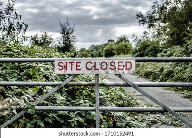 High Contrast View Of A Site Closed Sign Seen Attached To A Metal Gate, At The Entrance To A Now Derelict Germ Warfare Plant. The Area Is Now Overgrown With Vegetation, The Road Leading A Stores.