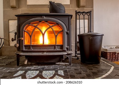 High efficiency cast iron wood stove burning firewood on a custom hearth constructed from black slate and white glass tile. A cast iron tea kettle humidifier sits on top of the stove.