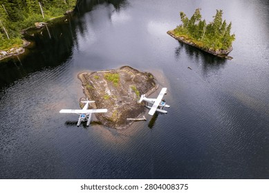 High elevated aerial close-up of floatplanes resting by a rocky islet in a serene high-altitude fjord lake in Misty Fjords National Monument.
