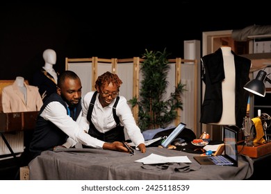 High end manufacturing suitmakers cutting textile material with scissors in tailoring studio, designing sartorial fashion clothes. Dressmakers working on bespoke client comission