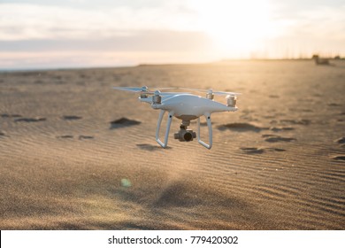 High end technology flying drone landing on sand at beach or desert during beautiful sunset or sunrise light. Tool for aerial footage for photographers and social media content creators