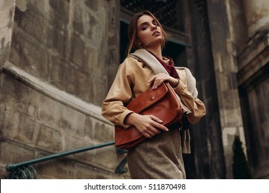 High Fashion Clothing. Beautiful Sexy Woman Wearing Fashionable Spring Or Fall Clothes ( Shirt, Scarf, Pants, Sweater, Leather Bag ) Outdoors. Female Model In Stylish Elegant Outfit Posing In Street