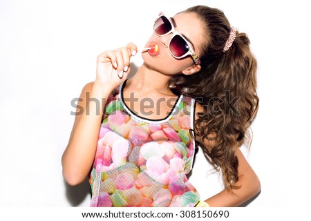 High fashion look.Glamor stylish beautiful young woman model with red lips in summer bright colorful hipster cloth,sunglasses,eat sweats.studio,eat lolly pop,isolated on white,candy woman,marshmallows
