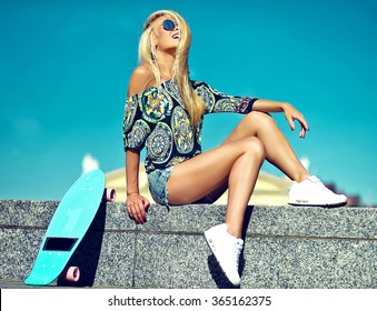 High Fashion Look.glamor Stylish Sexy Beautiful Young Cute Blond Model Girl In Summer Bright Casual Hipster Clothes With Skateboard Sitting Behind Blue Sky 