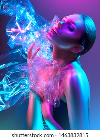 High Fashion model girl in colorful bright neon lights posing in studio through transparent film. Portrait of beautiful sexy woman in UV. Art design colorful make up. On colourful vivid background