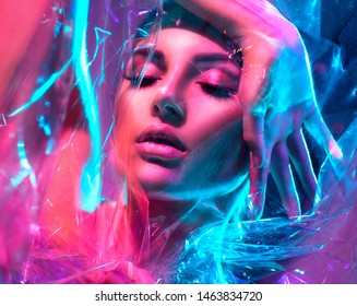 High Fashion Model Girl in bunten, leuchtenden Neonleuchten posieren im Studio durch transparenten Film. Portrait von schönen sexy Frau in UV. Kunstdesign bunter Make-up. Auf buntem, lebendigem Hintergrund