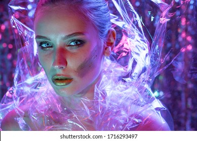 High Fashion model girl in colorful bright neon lights posing in studio through transparent film. Portrait of beautiful sexy woman in UV. Art design colorful make up. On colourful vivid background.