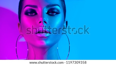 High Fashion model metallic silver lips and face woman in colorful bright neon uv blue and purple lights, posing in studio, beautiful girl, glowing make-up, colorful make up. Glitter Vivid neon makeup