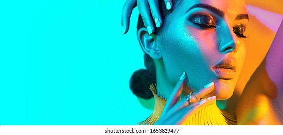 High Fashion model woman in colorful bright lights, portrait of beautiful sexy girl with trendy make-up and manicure. colorful neon skin, Art design, multicolor make up. Over blue background