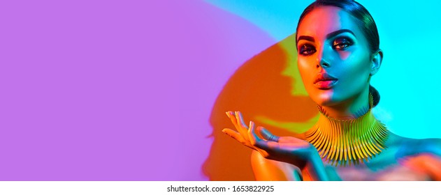 High Fashion model woman portrait in colourful bright neon lights, beautiful party girl with trendy make-up, manicure, hairstyle. Pointing hand, advertising gesture over colorful vivid background.