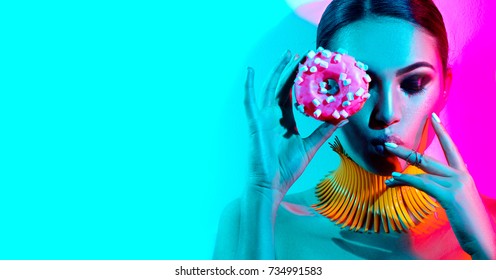 High Fashion Model Woman Posing In Studio With Donut In Colorful Bright Lights, Portrait Of Stylish Party Girl With Trendy Make-up, Haircut. Art Design Colorful Make Up. On Colourful Vivid Background.