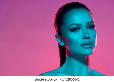 High fashion model woman's face in colorful bright neon UV blue and purple lights. Beautiful girl posing in the Studio, glowing makeup, colorful makeup. Glitter bright neon makeup. 