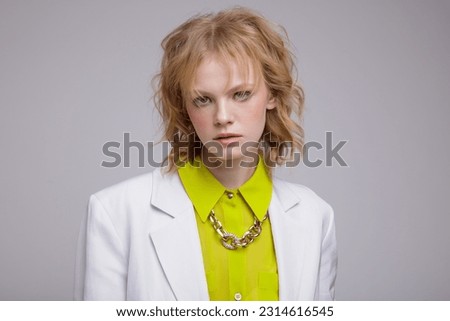 High fashion photo of beautiful elegant young woman in a pretty acid yellow shirt, shorts, jacket, blazer posing over white, soft gray background. Studio Shot, portrait. Blonde