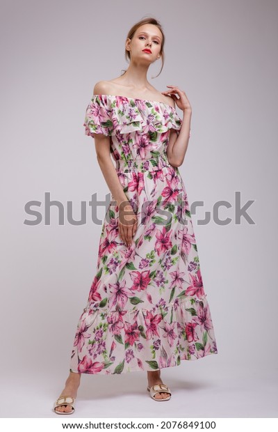 High fashion photo of a beautiful elegant\
young woman in  pretty long dress with floral patterns in red color\
posing over white, soft gray background. Slim figure.  Studio Shot.\
Femininity, tenderness